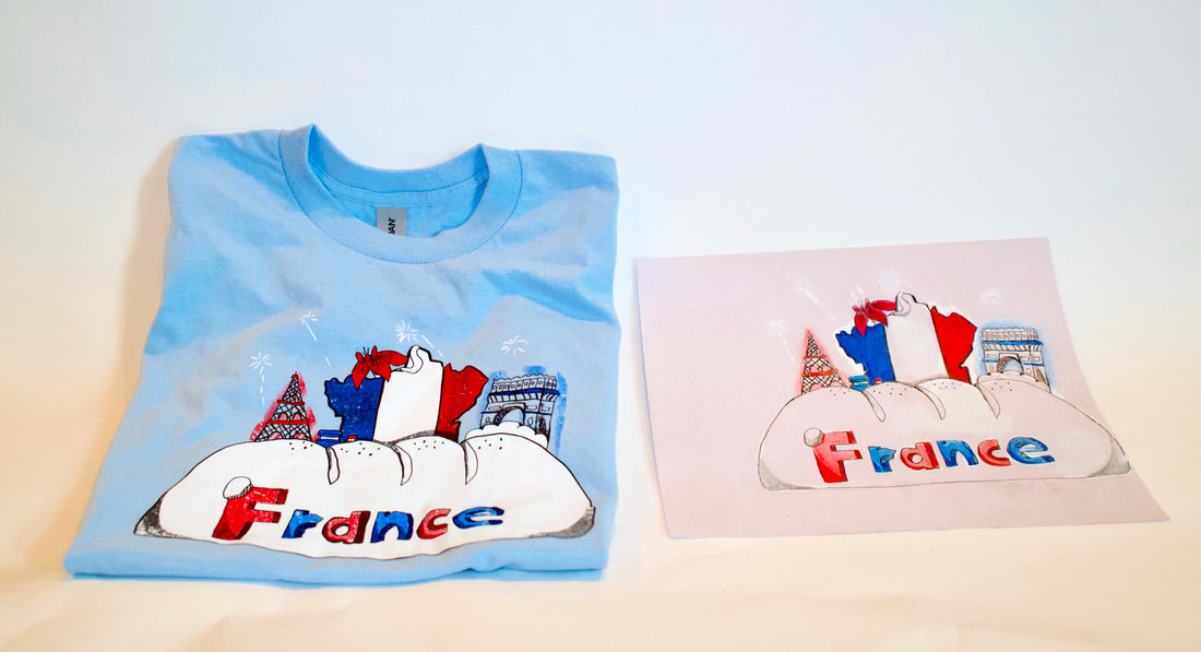 A blue t-shirt with screen printed image of the word France on a white cloud with the French flag colors with a drawing of the Eiffel Tower on the left and a drawing of the Arc de Triomphe on the right